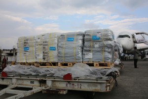 UNICEF relief supplies are stacked on pallets at Tribhuvan International Airport in Kathmandu, the capital. The UNICEF logo is on the shipment, which includes tents, tarpaulin sheeting, family hygiene kits and water purification tablets. More than 100 pallets of UNICEF relief supplies have been airlifted to the capital to date. A man and two workers stand near the shipment and an aeroplane on the tarmac. On 29 April 2015 in Nepal, search, rescue and relief operations continue in the aftermath of the massive 7.8-magnitude earthquake that hit the country on 25 April. The quakes epicentre was 80 kilometres from Kathmandu, the capital. Nearly 5,000 people have been killed, more than 9,700 others have been injured, and more than 8 million people have been affected. In the areas hardest hit by the disaster, about 1.7 million children urgently need humanitarian aid. Residences, schools and vital infrastructure, including hospitals, have been severely damaged or destroyed, leaving thousands of children and families homeless, vulnerable to disease outeaks and in urgent need of food, shelter, safe water and sanitation, and health support. Over 1.4 million people are in need of food assistance. Tens of thousands of displaced people are sheltering in camps or in available open spaces. The situation has been exacerbated by continuing powerful aftershocks that have caused additional damage. Working with the Government and other partners, including fellow United Nations organizations, UNICEF is supporting water, sanitation and hygiene (WASH), health, nutrition, child protection, education and other interventions. In response to the disaster, UNICEF is providing tents, including for hospitals; tarpaulin sheeting; emergency medical kits; vaccines and related supplies; zinc and oral rehydration salts to prevent diarrhoeal disease outeaks; water purification tablets; hygiene kits and buckets; and temporary learning spaces and psychosocial counselling for children. UNICEF is