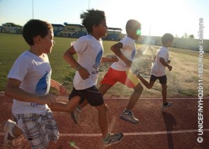 Boys run on a track at Guillermo Prospero Trinidad Stadium, in Oranjestad, the capital. They are participating in a programme offered by Athletik Bond, a local government-sponsored organization that coaches children in track and field sports.  In September 2011, Aruba continues working to protect the welfare of its children since gaining autonomy from the Netherlands in 1986. Nevertheless, Aruba, like its sister islands in the Caribbean  Curacao and the Dutch portion of Sint Maarten  remains part of the Kingdom of the Netherlands, bound by its international treaties, including the Convention on the Rights of the Child (CRC). To assess the status of Arubas children, UNICEF was invited to undertake a situation analysis  UNICEFs core methodology to define child welfare in a given country, reviewing childrens situation in the context of an array of social, economic, political, institutional and historic factors. The aim was to evaluate progress and challenges in realizing childrens and womens rights in Aruba and to make recommendations for policies and social actions to improve these conditions. The analysis noted Arubas generally favourable economic status but also its high dependency on tourism, which provides limited employment options for islanders and makes them highly vulnerable to steep downturns in the global economy. It also showed the benefits of the islands universal health care: over 99 per cent of women receive antenatal care; more than 95 per cent of births are overseen by skilled attendants; vaccination coverage among children between 12 and 23 months old has reached 90 per cent, and all children have access to safe drinking water and improved sanitation facilities. Nevertheless, obesity affects 35 per cent of children, heralding future health problems, and rising rates of adolescent pregnancy are causing increased health and social complications. In education, nearly all children aged 611 years attend primary school. However, the absence of laws requiring post-secondary attendance contributes to high dropout rates for adolescents, which, in turn, contributes to the numbers of youth involved in gangs or substance abuse. Current policy also mandates Dutch  in which only 5.8 per cent of the population is fluent  as the principal language of instruction, instead of Papiamento, a Creole language spoken by 66.3 per cent of inhabitants. Language barriers are compounded for the 30 per cent of the population who are new immigrants, most of whom speak neither Dutch nor Papiamento. A preponderance of low-wage jobs and inadequate childcare also contribute to rising reports of child abuse. UNICEF recommendations note the need for a more diversified economy that promotes social welfare as well as growth and for continued reporting and visibility for childrens issues to support positive change. It also recommends improved interaction and coordination between state, social, private and union sectors to implement policies addressing the language of educational instruction, high school attendance, childhood obesity, protections against abuse and domestic violence, as well as the needs of diverse cultures.