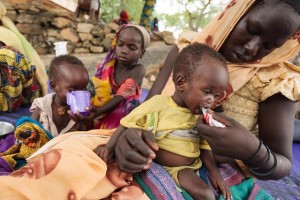 (Foreground) Mariam, 15, feeds her 10-month-old sister, Fatouma, from a package of Plumpynut, at the UNICEF-supported outpatient feeding centre in the town of Bitkine, Guera region. Plumpynut, a and of ready-to-use therapeutic food, is a high-protein, high-energy, peanut-based, packaged paste for malnourished children that does not require cooking or handling. Behind them, Aljema, 8, feeds another type of therapeutic food to Toma, her younger sister.