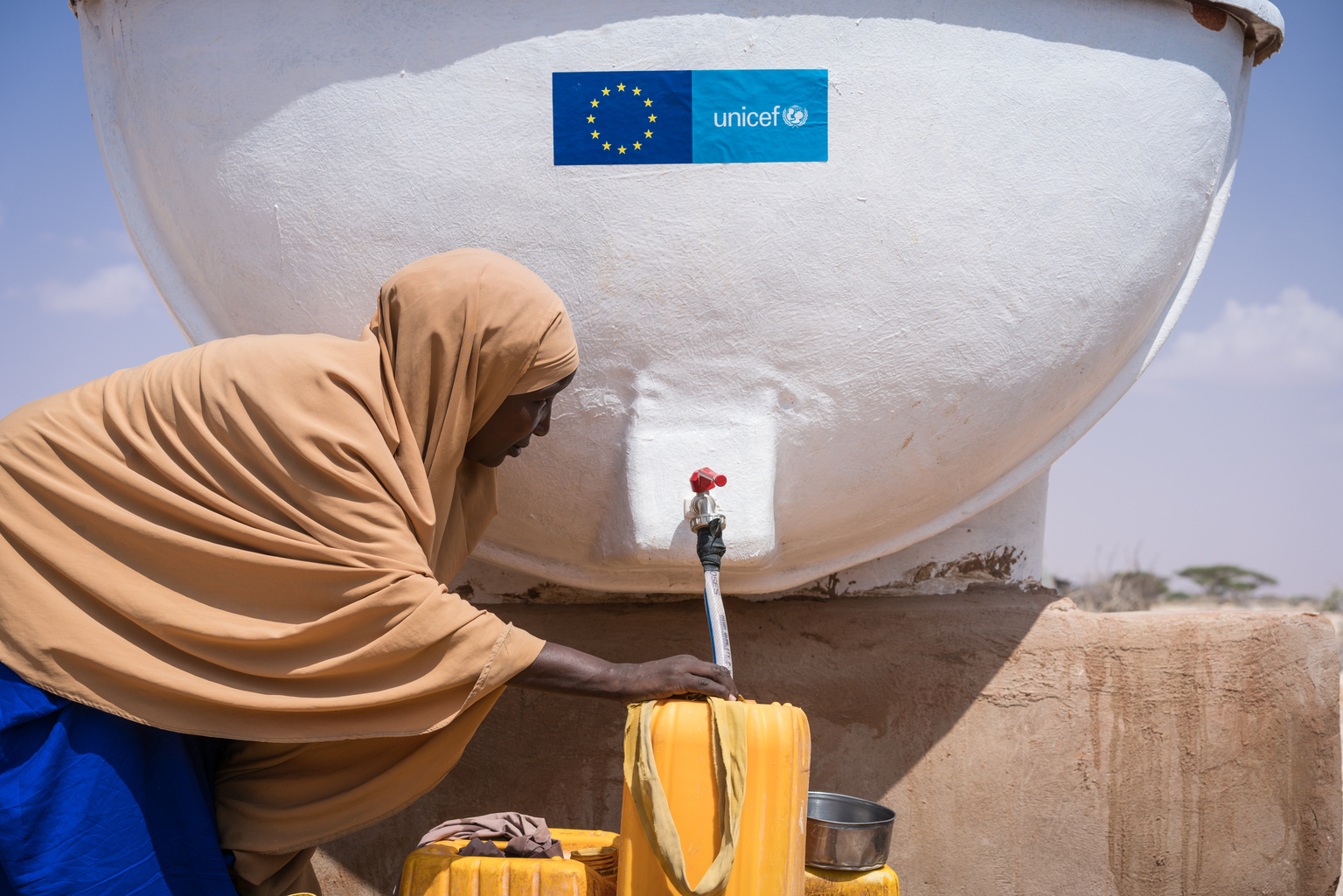 A young woman displaced from her home by the worsening drought fills containers with clean water to carry back to her new home in the internally displaced peoples camp in Galkayo, Somalia, Wednesday 12 April 2017. As of April 2017, the humanitarian situation in Somalia continues to deteriorate due to the severe drought, which started in the north in 2016 and is now affecting most of the country. Over 6.2 million people are facing acute food insecurity and 4.5 million people are estimated to be in need of water, sanitation and hygiene (WASH) assistance. The situation is especially grave for children. Close to one million children (under five) will be acutely malnourished in 2017, including 185,000 severely malnourished, which may increase to over 270,000 if famine is not averted. Severely malnourished children are nine times more likely to die of killer diseases like cholera / acute watery diarrhea and measles, which are spreading. The drought is also uprooting people, with more than 530,000 displaced since November 2016, adding to the 1.1 million already internally displaced (IDPs). This includes 278,000 new IDPs in the month of March alone, with 72,000 new arrivals in Mogadishu and 70,000 in Baidoa. In addition, the number of people crossing into Kenya is increasing. The rapid scale of displacement increases the risk of family separation and gender-based violence. Children are also dropping out of school, with 50,000 children reported to have stopped going to school, and an additional 40,000 at risk of being forced to interrupt their schooling. The Gu (April-June) rains are slowly unfolding, inging much needed relief to parts of the country. But the rains also spell danger for children. If they come in full they will inflict further misery on children living in flimsy, makeshift shelters made of twigs and cloth or tarps. If the Gu rains fail, and if assistance doesn’t reach families, more people will be forced off their land into displacement camps. Out